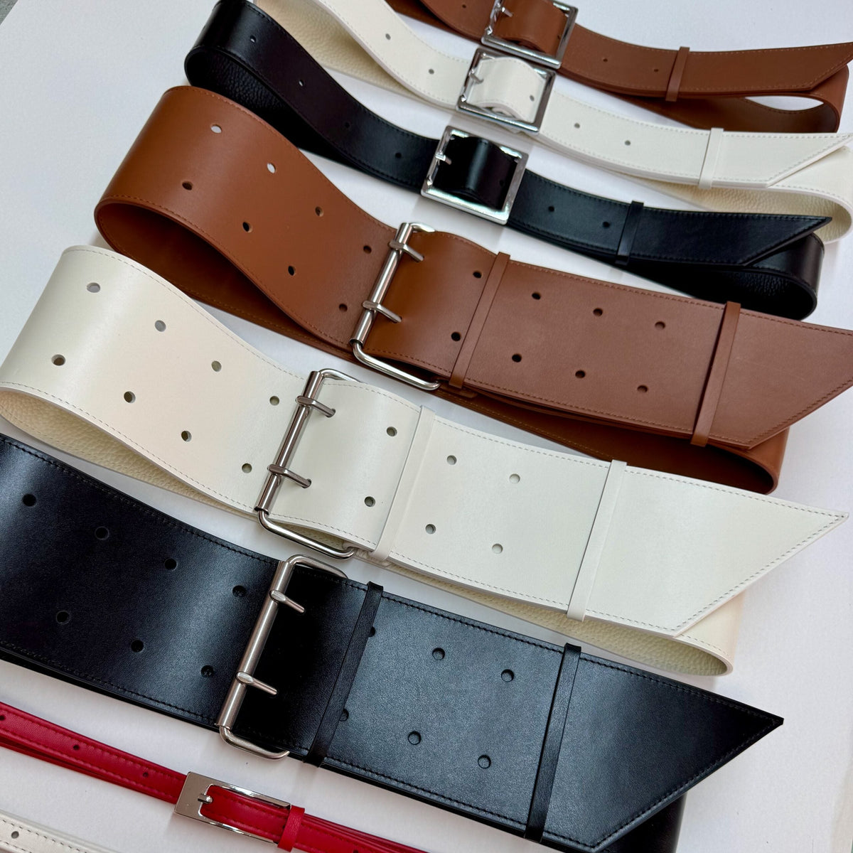 Aria Margo wide leather military belts in off-white, black, brown, and red with silver double-prong buckles.