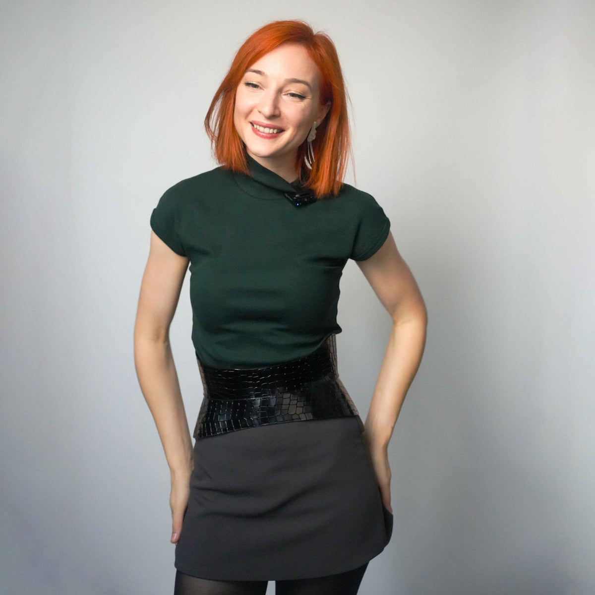 Aria Margo Test black croc-embossed leather hourglass corset belt worn over a dark green top and grey skirt