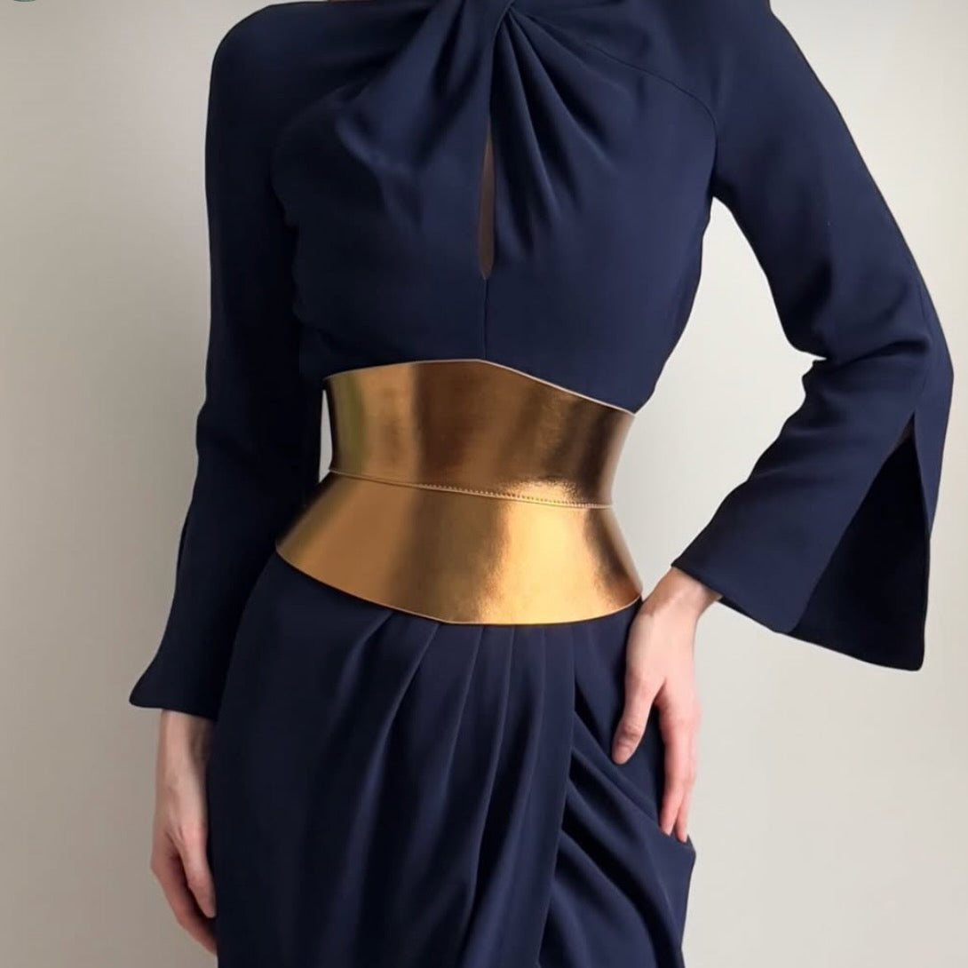 Aria Margo gold metallic Italian leather corset belt with an hourglass silhouette worn over a navy blue dress.
