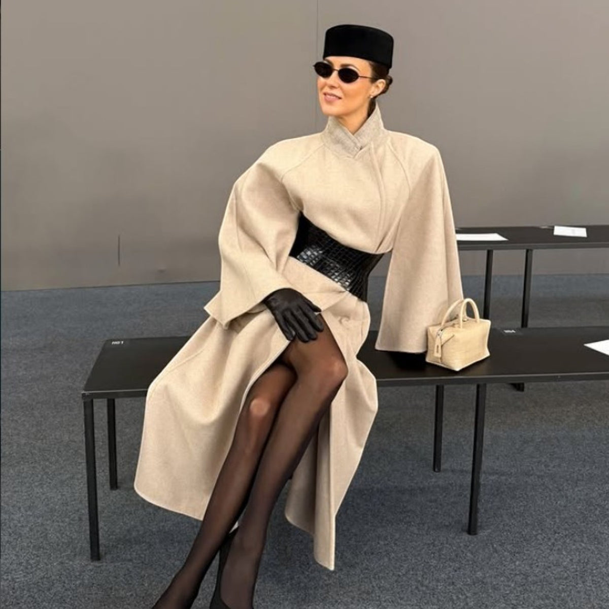 Aria Margo black croc-embossed leather hourglass corset belt worn over a beige wool coat by a seated model