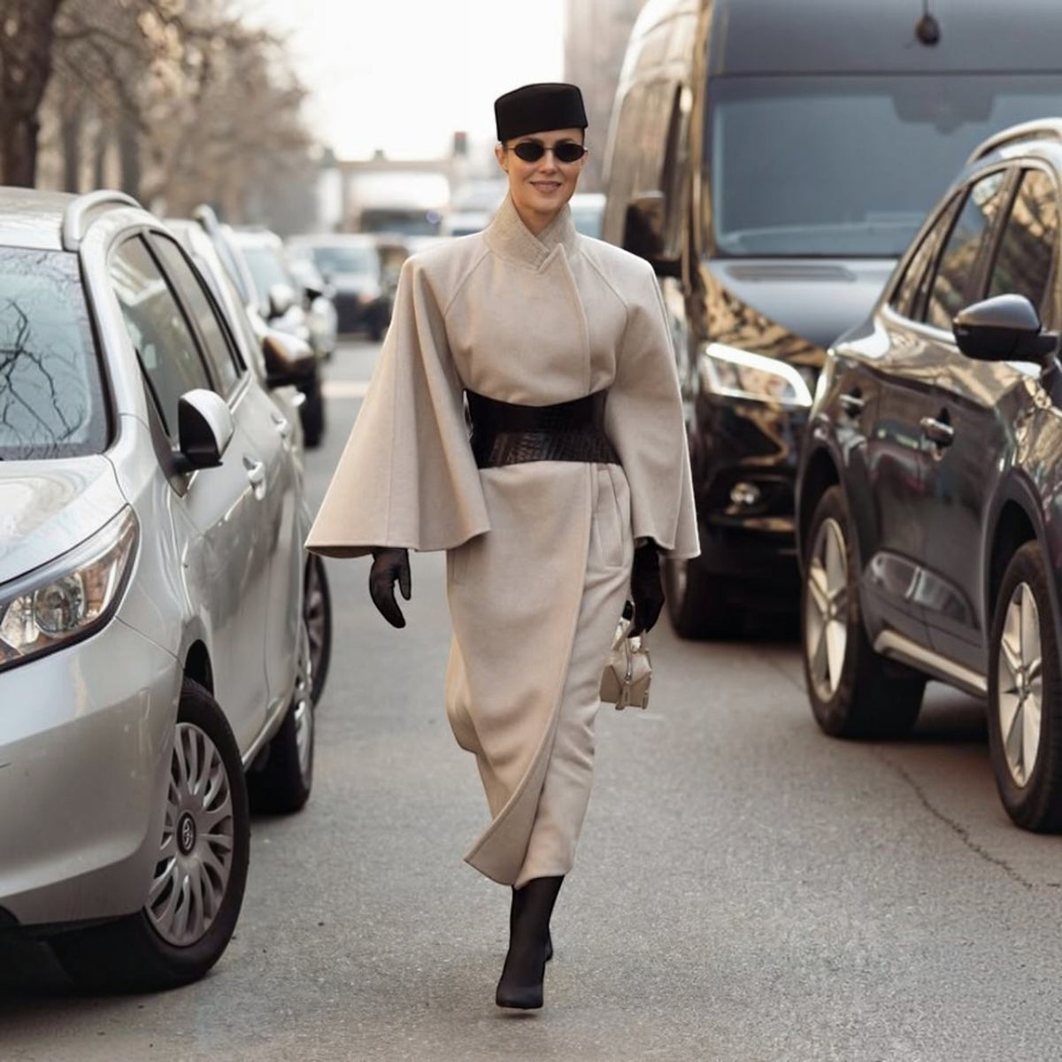 Aria Margo black croc-embossed leather hourglass corset belt worn over a beige wool cape coat on a city street.