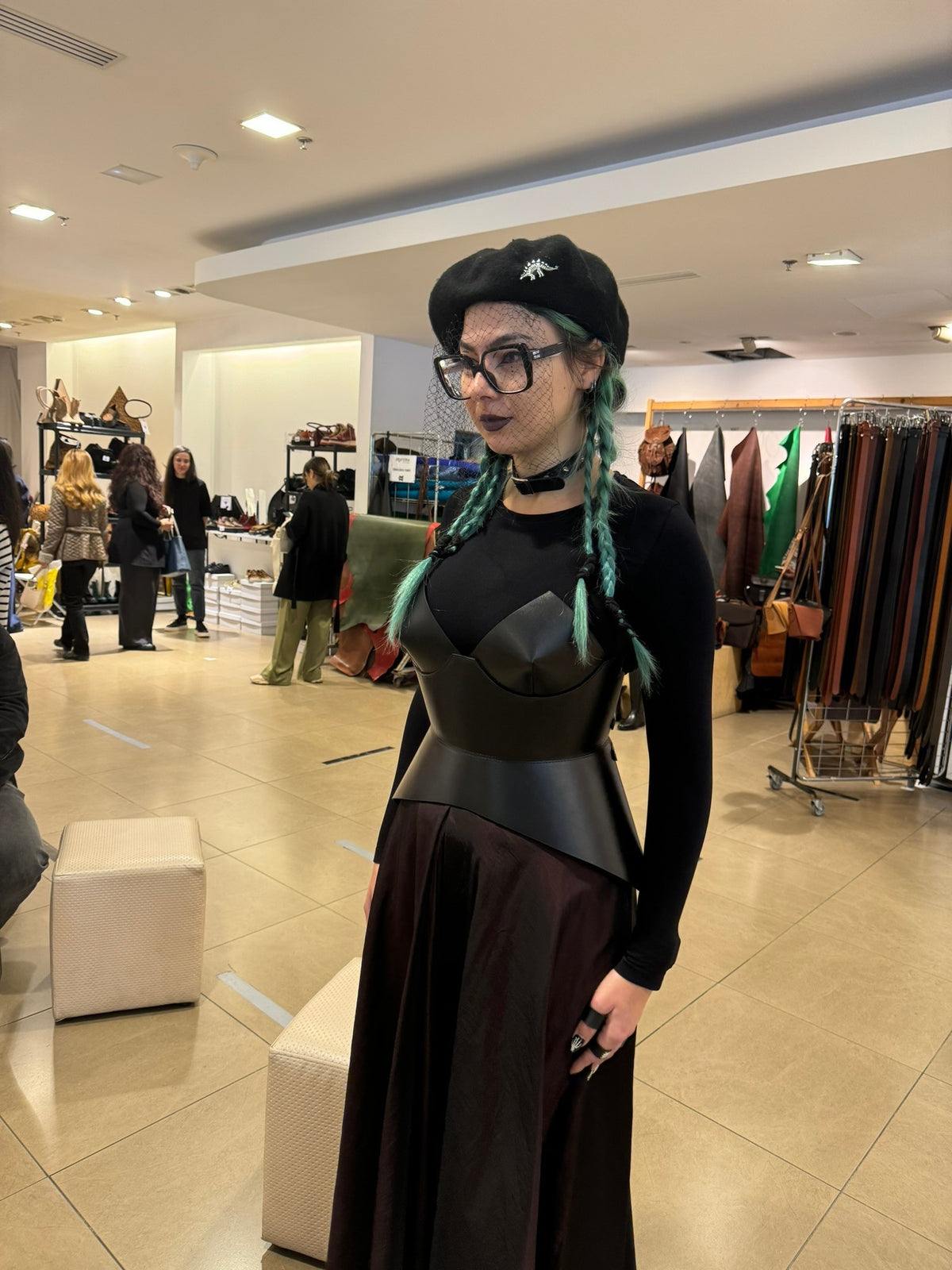 Aria Margo black leather full body corset belt worn over a black long-sleeve top and skirt in a boutique store.