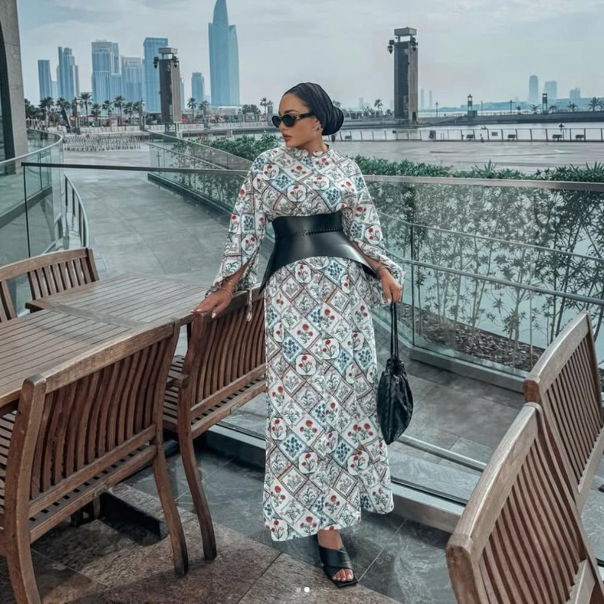 Aria Margo black leather corset belt worn over a patterned maxi dress by a woman in an outdoor city setting.