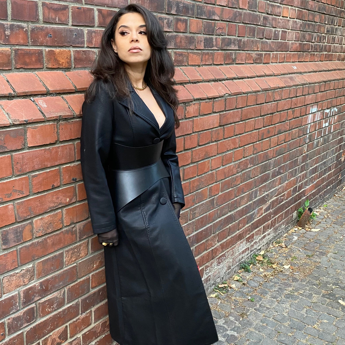 Aria Margo black leather corset belt worn over a long black coat, highlighting a feminine silhouette.