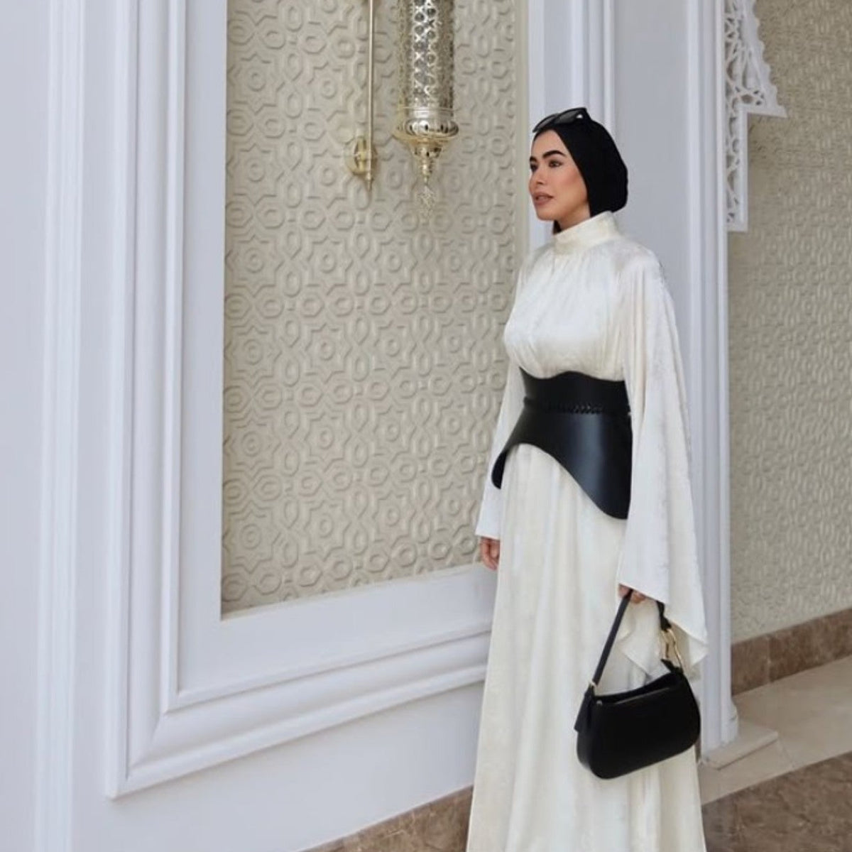 Aria Margo black leather corset belt worn over a white long-sleeved dress, creating a sculpted hourglass silhouette