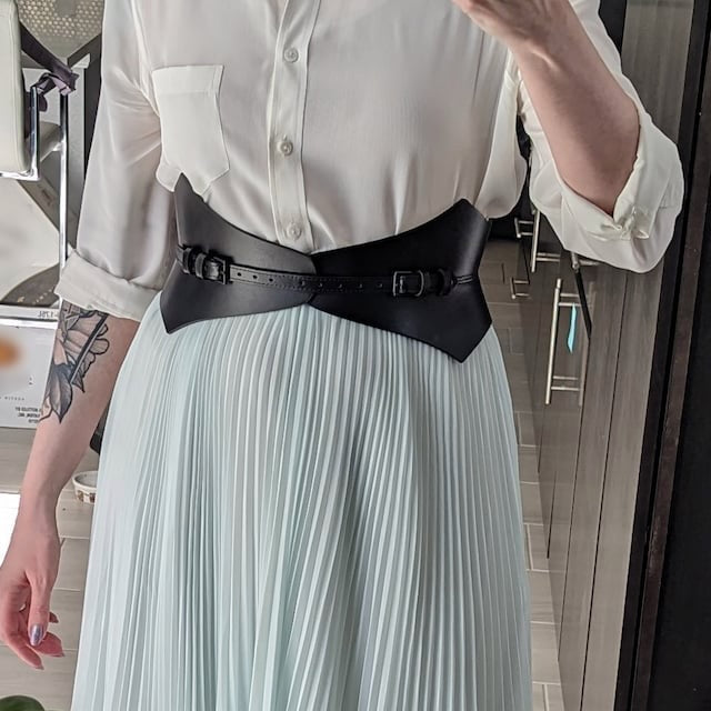 Aria Margo black Italian leather corset belt with pointed edges worn over a white shirt and pleated skirt
