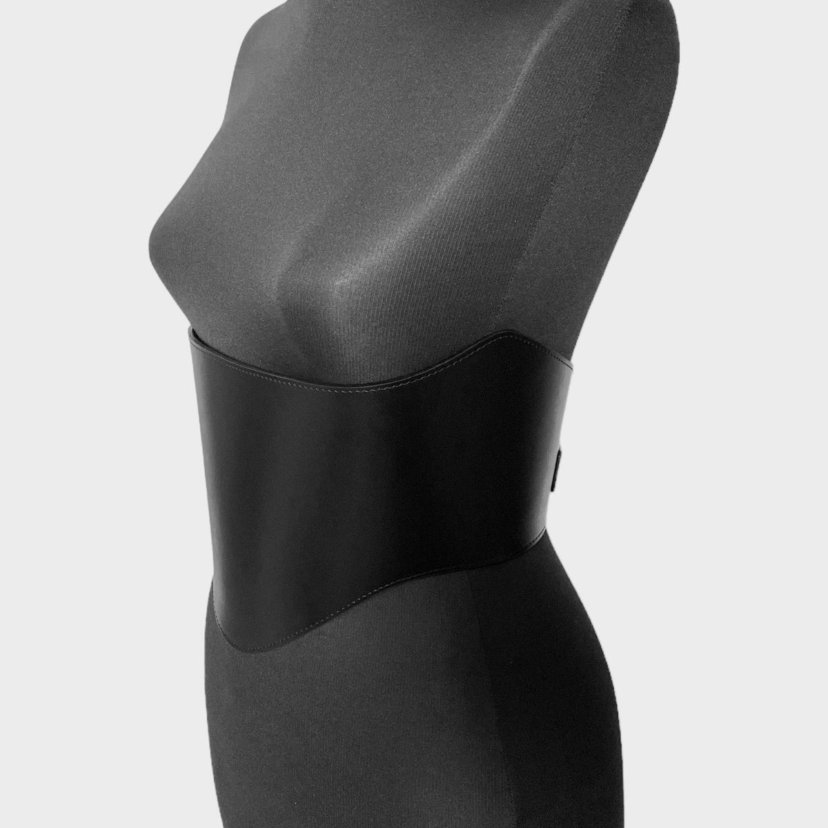 Aria Margo black leather under-bust belt with a curved design on a mannequin, providing waist definition.