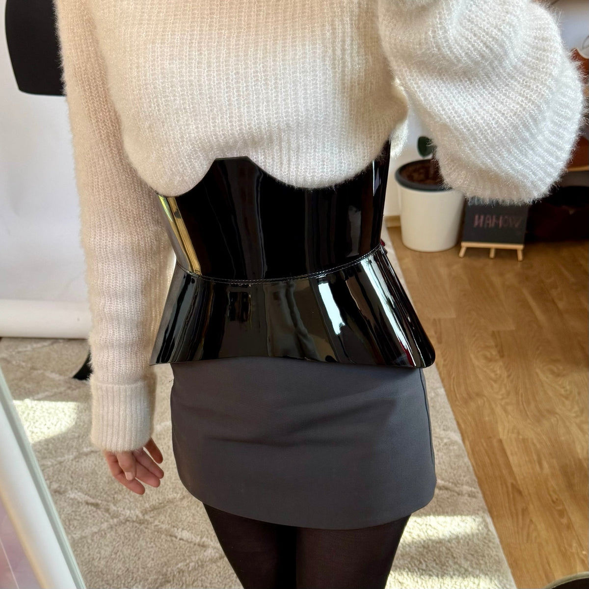 Aria Margo black patent leather corset belt with a sculpted hourglass shape worn over a white fuzzy sweater
