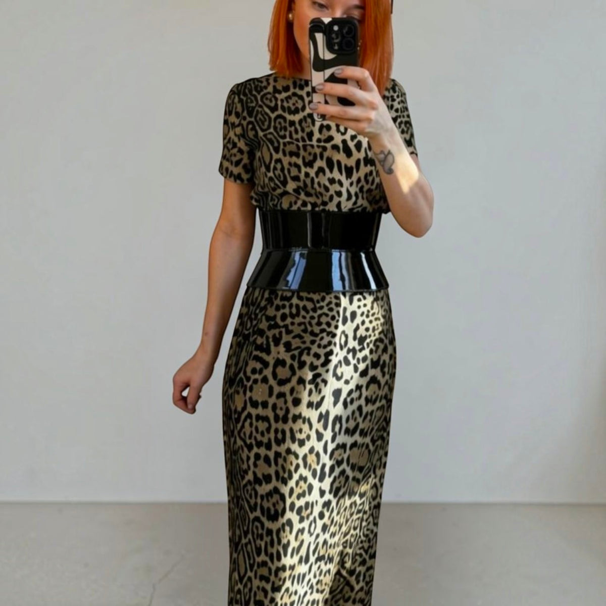 Aria Margo wide black patent leather corset belt worn over a leopard print dress for a defined hourglass shape.