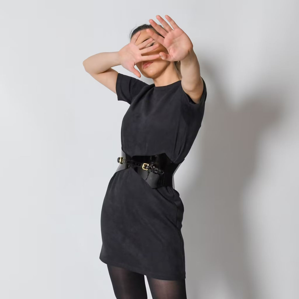 Aria Margo black patent leather corset belt worn over a black dress, highlighting the waist with a high-shine finish