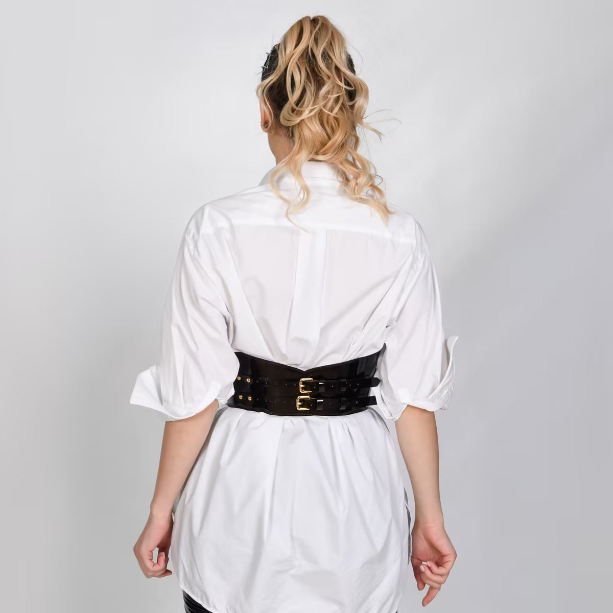 Aria Margo  black patent leather under-bust belt with double buckles worn over a white button-down shirt, back view