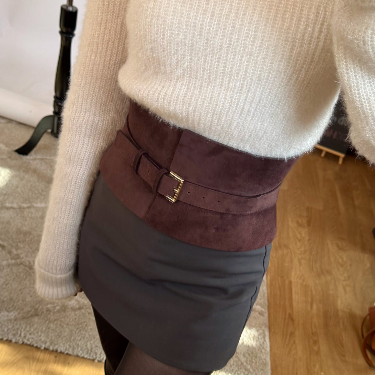 Aria Margo wide brown suede corset belt worn over a white knit sweater and dark skirt for a defined waistline