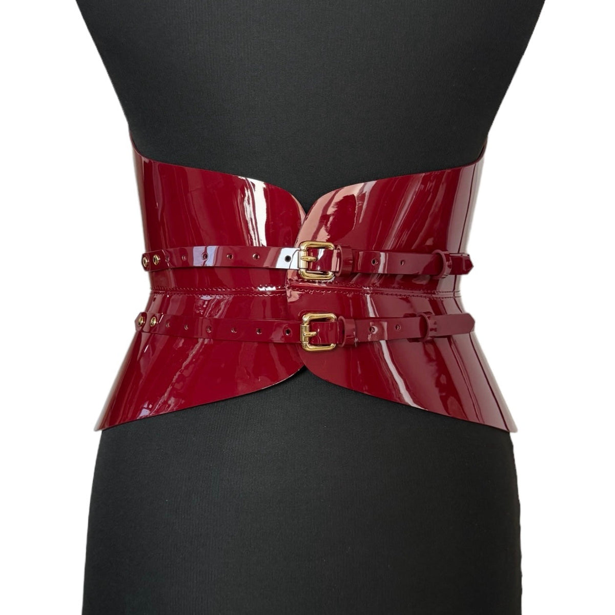 Aria Margo burgundy patent leather corset with a high-shine finish, featuring two gold buckles on a mannequin.