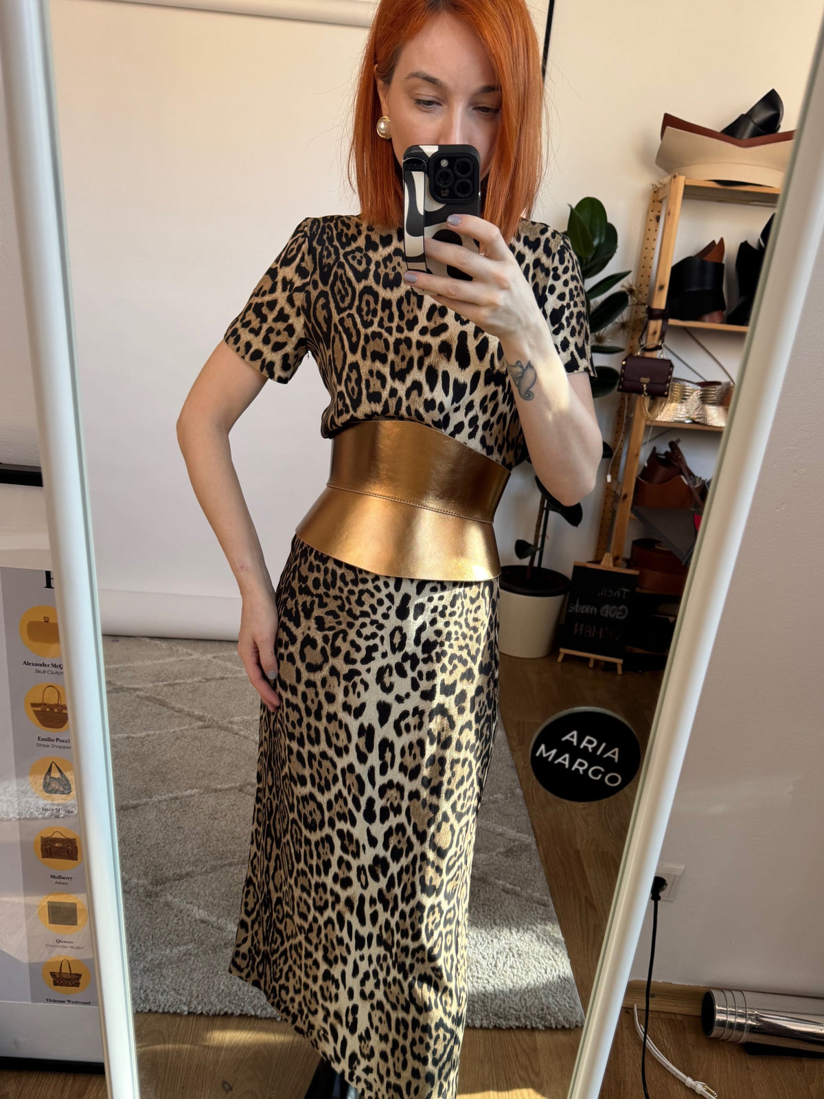 Aria Margo Eclipse gold leather corset belt worn over a leopard print dress in a mirror selfie