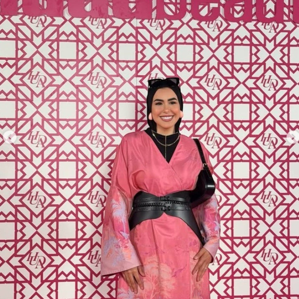 Aria Margo Nova black leather corset belt worn over a pink patterned dress by a smiling woman in a hijab.
