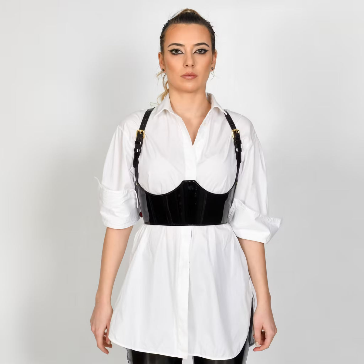 Aria Margo black patent leather under-bust belt with adjustable straps worn over a crisp white button-down shirt.