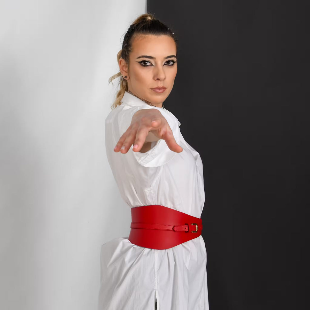 Aria Margo slim red Italian leather corset belt worn over a white shirt dress against a split black background.