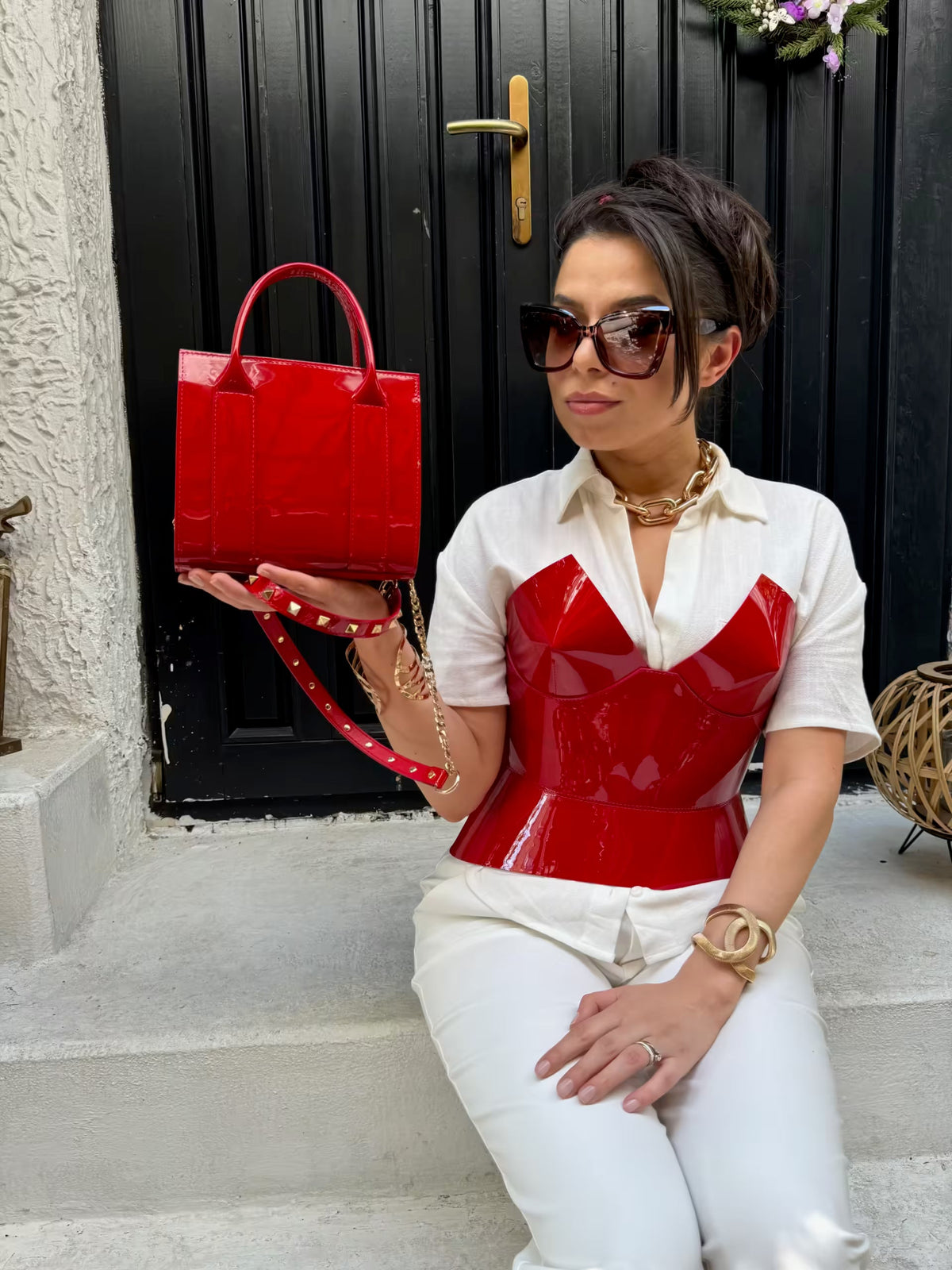 Aria Margo red patent leather corset worn over a white shirt with a matching red patent handbag