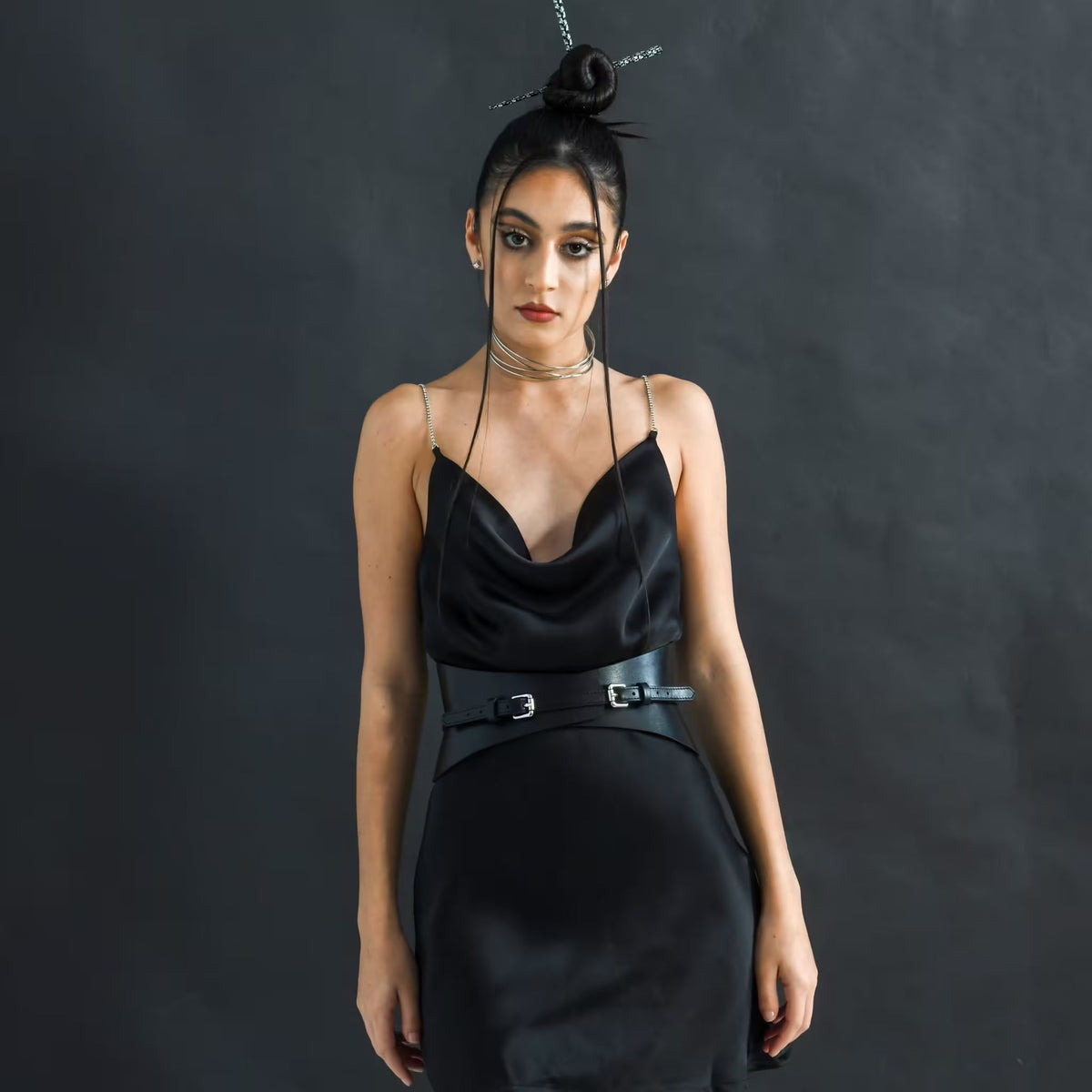 Aria Margo slim black leather corset belt worn over a matching black satin cowl neck dress