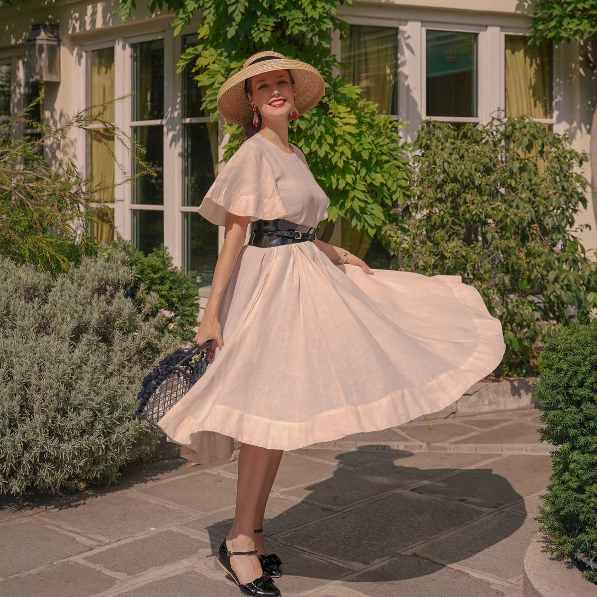 Aria Margo slim black patent leather corset belt worn by a woman in a beige dress in a garden setting.