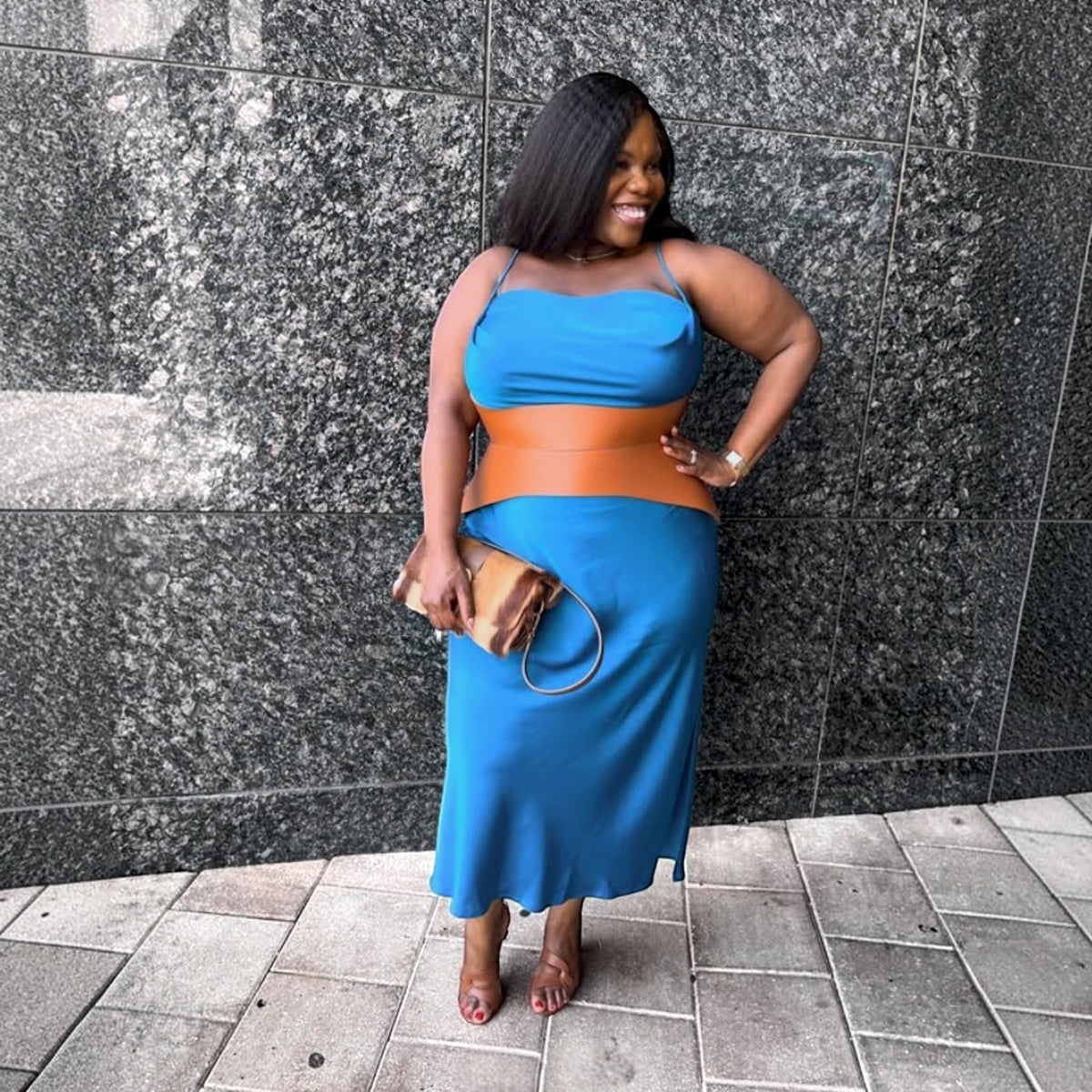 Aria Margo Test brown leather corset belt worn over a blue midi dress by a smiling woman standing against a wall.