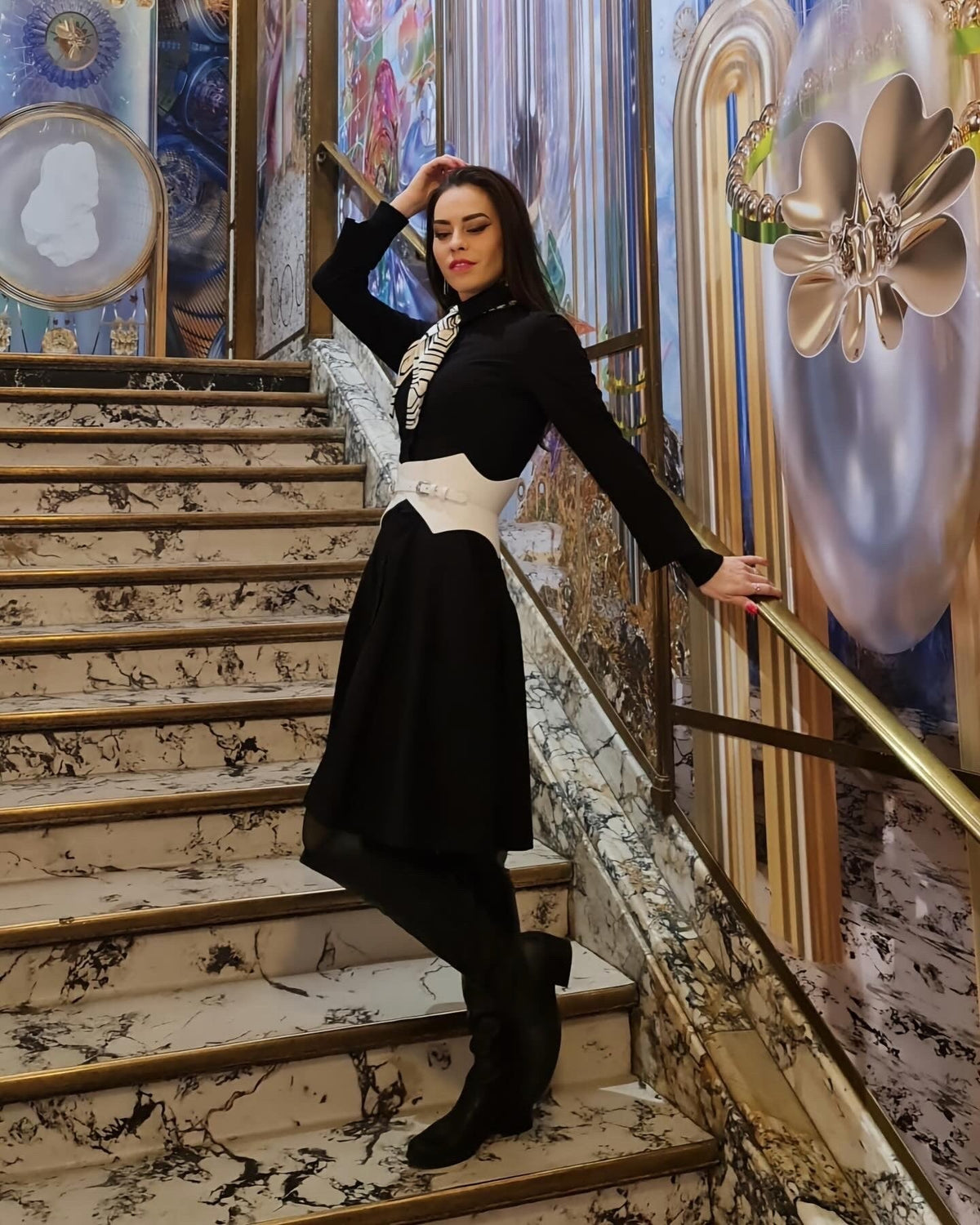 Aria Margo white leather corset belt worn over a black dress by a model standing on a marble staircase