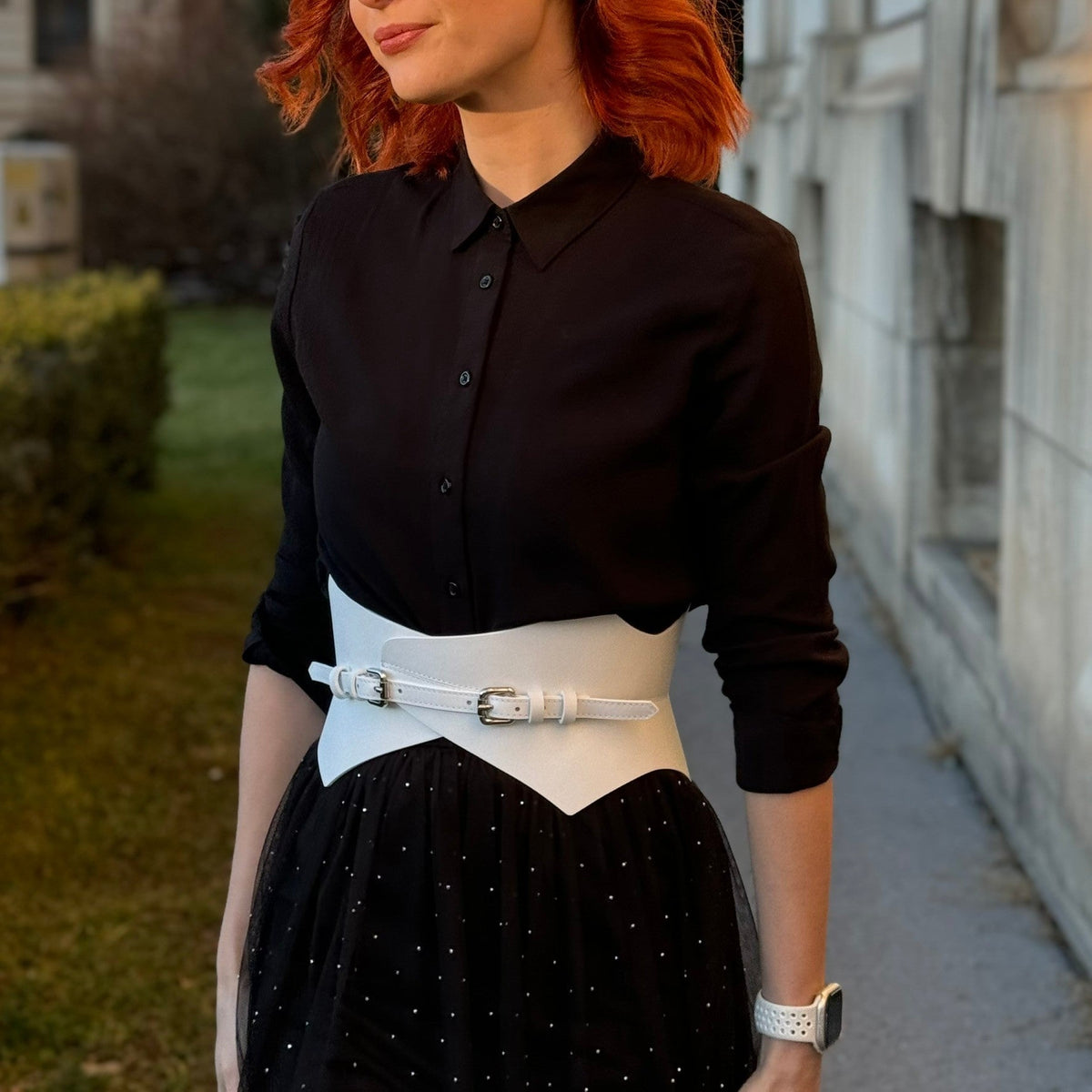 Aria Margo white leather corset belt worn over a black button-down shirt and skirt, highlighting waist shape.