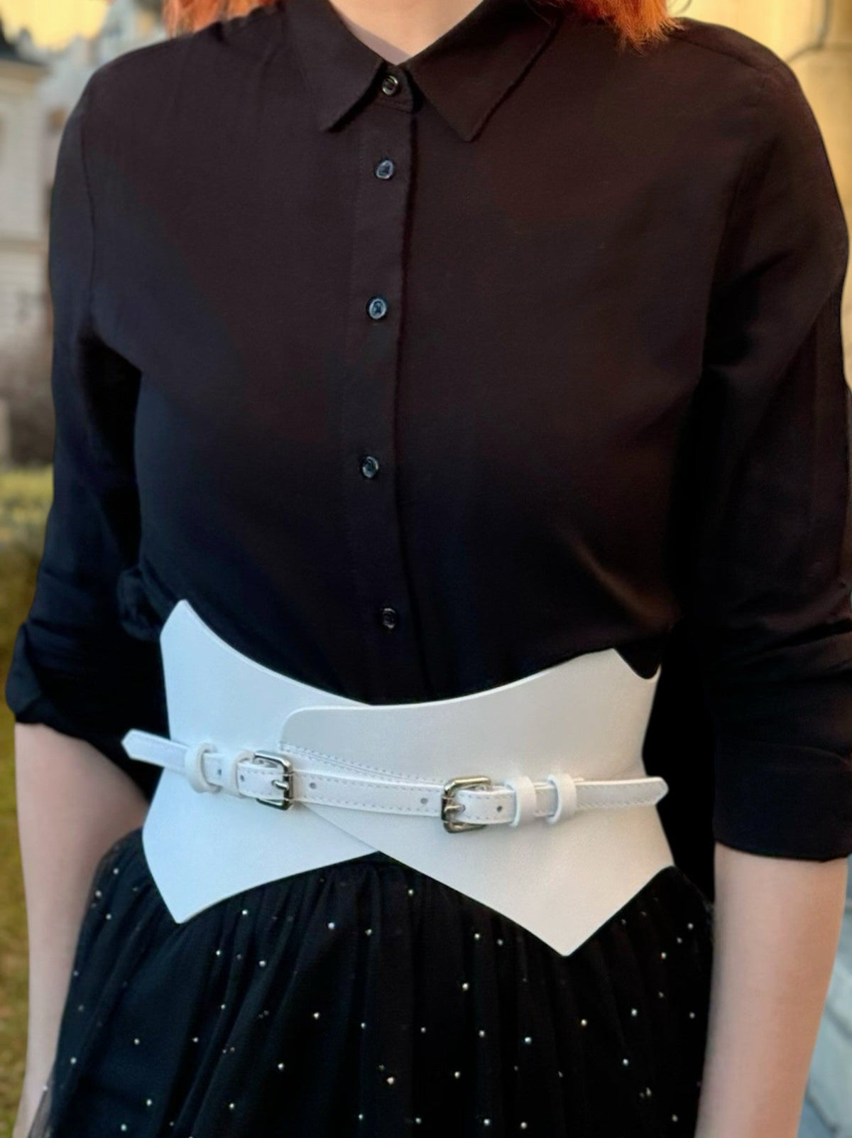 Aria Margo white leather Thorns corset belt worn over a black button-down shirt by a woman with red hair