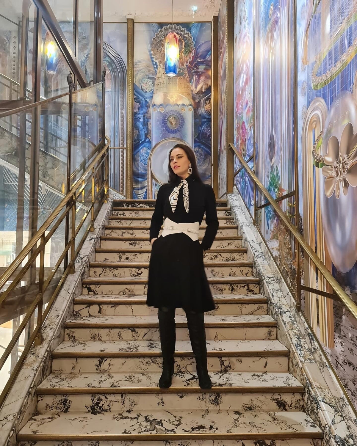 Aria Margo white leather Thorns corset belt worn over a black dress by a woman standing on a grand staircase.